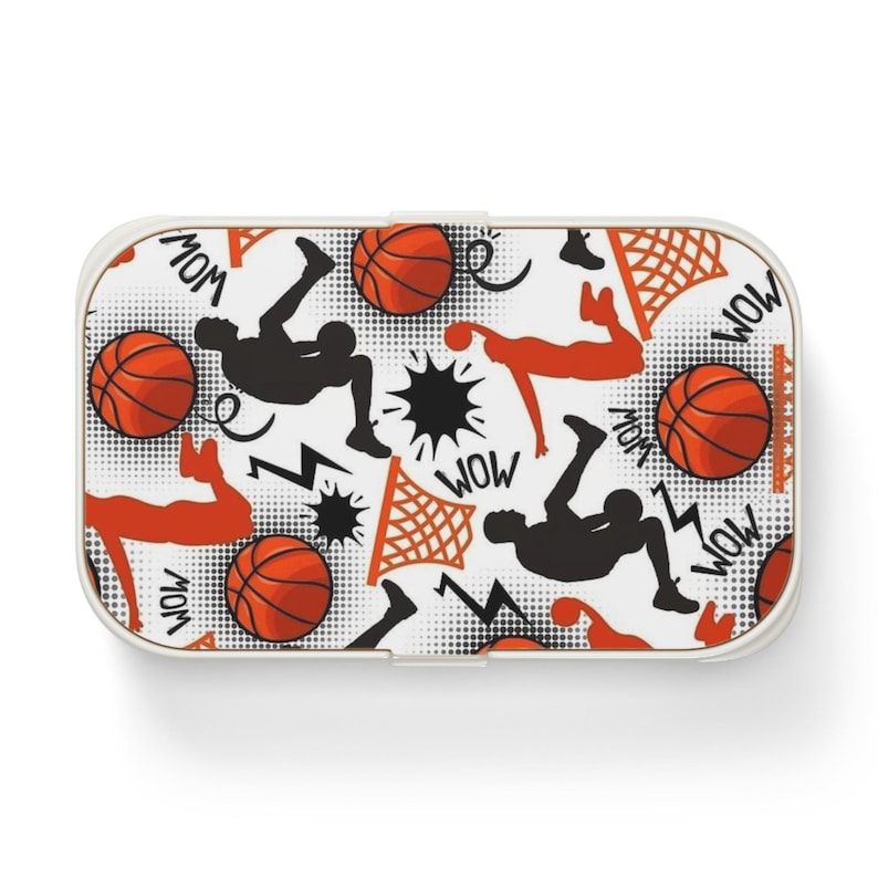 May include: A rectangular lunch box featuring a white background with a repeating basketball-themed pattern. The design includes orange basketballs, black and orange silhouettes of players, basketball hoops, lightning bolts, and the word WOW.