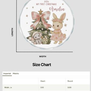 May include: A round, clear glass Christmas ornament featuring a printed illustration of a rabbit and an elephant near a decorated tree. The text reads 2026 MY FIRST CHRISTMAS Amelia. The ornament has a red ribbon hanger and measures 7.62 cm.
