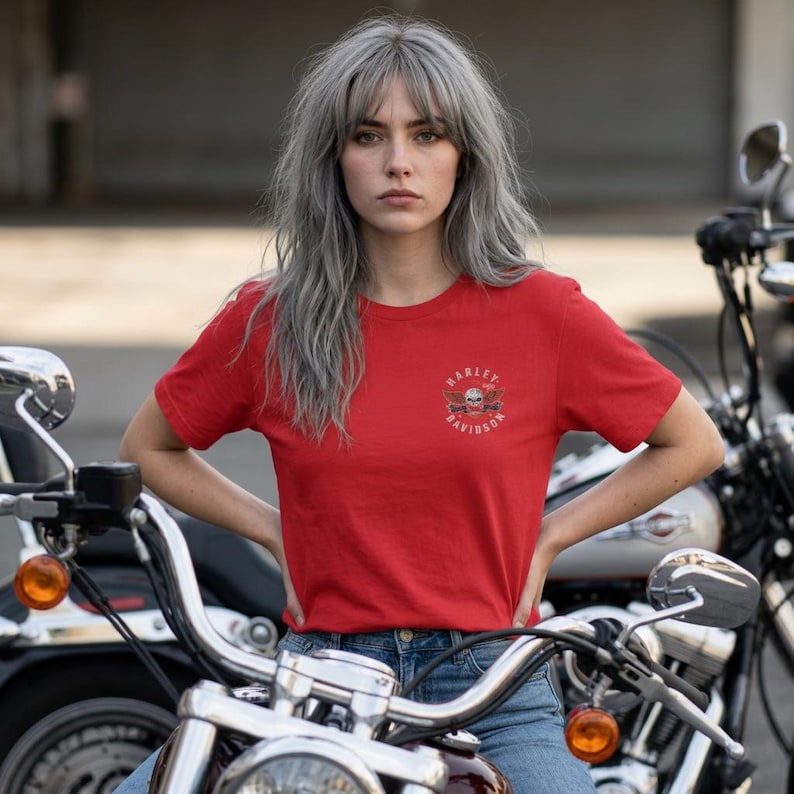 K&ouml;nnte beinhalten: Ein leuchtend rotes Kurzarm-T-Shirt mit einem kleinen Harley-Davidson-Logo auf der linken Brust. Das Logo zeigt eine Grafik eines Totenkopfes mit Fl&uuml;geln und den Schriftzug Harley-Davidson in kreisf&ouml;rmiger Anordnung. Mit Rundhalsausschnitt.
