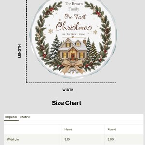 May include: A round, clear glass Christmas ornament featuring a printed wreath of pine branches, pinecones, and red berries surrounding a house illustration. Text reads: The Brown Family, Our First Christmas in Our New Home, 2026. Width 3.00 inches.