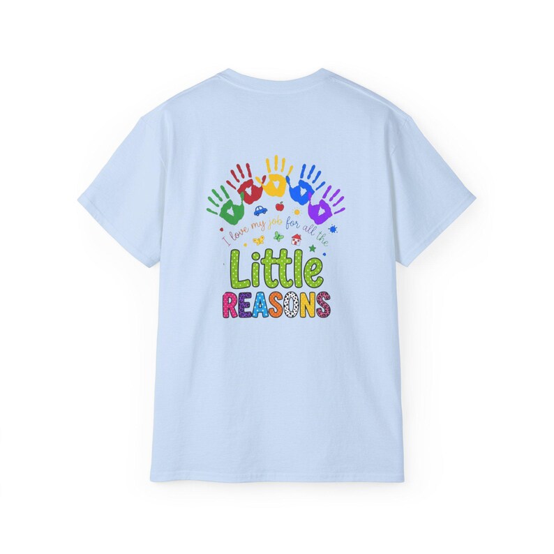 May include: A light blue t-shirt featuring a colorful graphic on the back. The design includes five handprints in green, red, yellow, blue, and purple, with the text "I love my job for all the Little REASONS" and small icons like a car and apple.