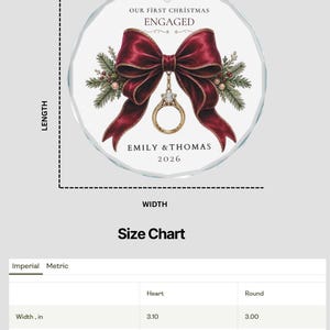 以下が含まれることがあります： 赤いリボンが付いた丸いガラス製のクリスマスオーナメント。濃い赤のリボン、金の婚約指輪、松の枝が描かれています。文字は「OUR FIRST CHRISTMAS ENGAGED, EMILY & THOMAS, 2026」。サイズは幅7.62cm、高さ7.62cmです。