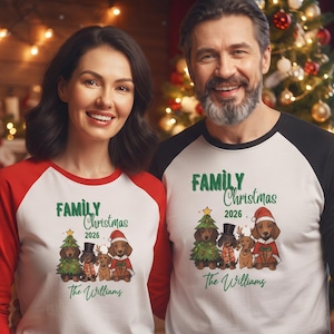 Op de afbeelding: Twee raglan-shirts met een witte romp en gekleurde mouwen. De shirts tonen een afbeelding van vier teckels in feestelijke kleding, de tekst "FAMILY Christmas 2026" en de naam "The Williams" in groen cursief schrift.