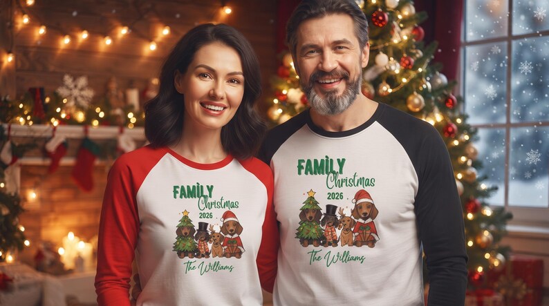 Op de afbeelding: Twee raglan-shirts met een witte romp en gekleurde mouwen. De shirts tonen een afbeelding van vier teckels in feestelijke kleding, de tekst "FAMILY Christmas 2026" en de naam "The Williams" in groen cursief schrift.