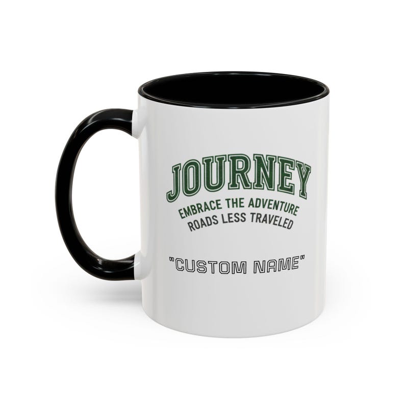 May include: White ceramic mug with a black handle and interior. The mug features the word "JOURNEY" in green, along with the phrases "EMBRACE THE ADVENTURE" and "ROADS LESS TRAVELED". The bottom of the mug reads "CUSTOM NAME".