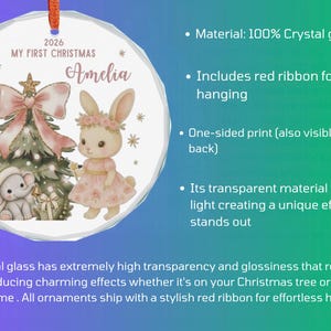May include: A round crystal glass ornament featuring a printed illustration of a Christmas tree, a small elephant, and a rabbit wearing a floral crown. The text reads 2026 MY FIRST CHRISTMAS and Amelia. A red ribbon is attached for hanging.