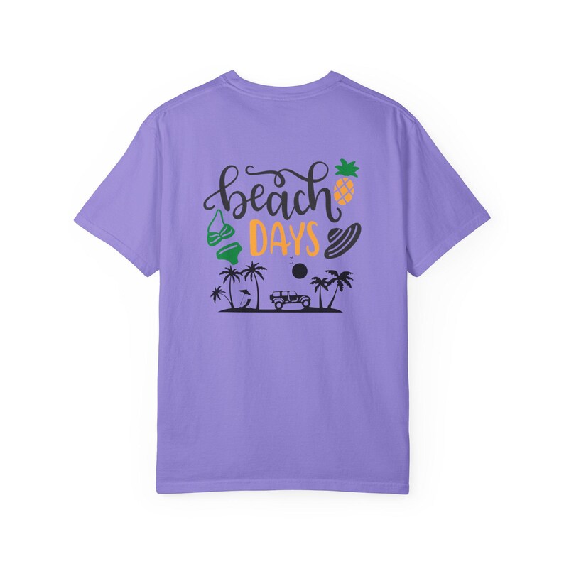 May include: A lilac-colored t-shirt with a graphic on the back that says "beach days". The graphic includes a pineapple, a bikini top, a sun, palm trees, a car, and a surfboard.