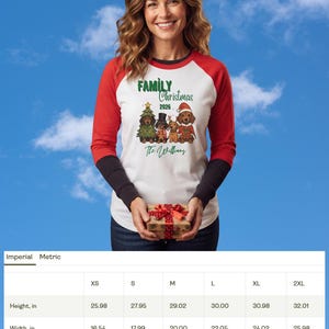 Op de afbeelding: Een wit raglan-shirt met rode mouwen en zwarte boorden met een afbeelding van vier teckels in feestelijke kleding. De tekst luidt Family Christmas 2026 en The Williams. Een maattabel toont de hoogte en breedte in inches voor maten XS tot 2XL.