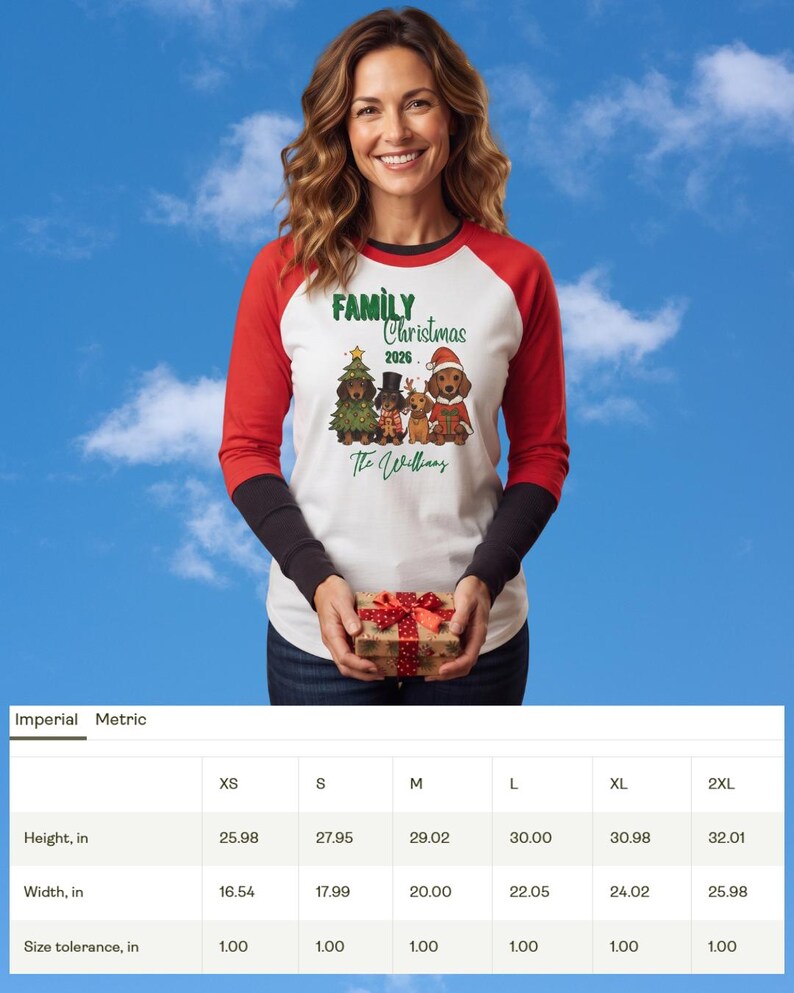 Op de afbeelding: Een wit raglan-shirt met rode mouwen en zwarte boorden met een afbeelding van vier teckels in feestelijke kleding. De tekst luidt Family Christmas 2026 en The Williams. Een maattabel toont de hoogte en breedte in inches voor maten XS tot 2XL.