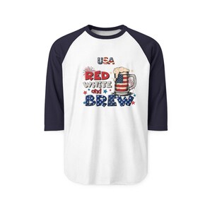 Peut inclure: Un t-shirt de baseball blanc &agrave; manches trois-quarts bleu marine avec un motif repr&eacute;sentant une chope de bi&egrave;re aux couleurs du drapeau am&eacute;ricain, le texte USA et les mots RED WHITE and BREW en rouge, blanc et bleu avec des &eacute;toiles.