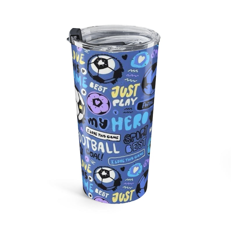 May include: A blue tumbler with a clear lid featuring a repeating pattern of soccer balls, hearts, and text including "JUST PLAY," "MY HERO," "FOOTBALL," "GOAL," and "I LOVE THIS GAME" in yellow, white, and light blue colors on a dark blue background.