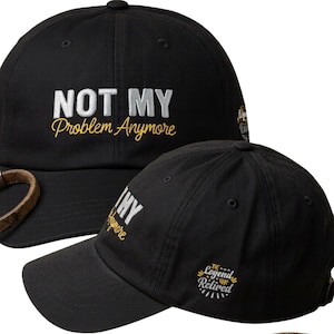 Op de afbeelding: Een zwarte honkbalpet met de wit en geel geborduurde tekst "NOT MY Problem Anymore" op de voorkant. De zijkant van de pet toont een cirkelvormig geborduurd embleem met de tekst "THE Legend HAS Retired" in het wit en geel.