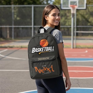 Może przedstawiać: Czarny plecak z grafiką pomarańczowej piłki do koszyk&oacute;wki nad białym napisem BASKETBALL. Poniżej znajduje się imię JESSICA, a pod nim pomarańczowy tekst WE ARE NEXT oraz słowo Generations zapisane ozdobną czcionką przypominającą pismo ręczne.