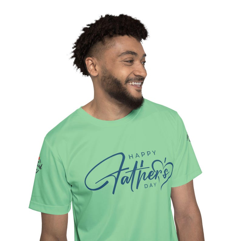 May include: A light green t-shirt with the words "Happy Father's Day" in a dark blue script. The shirt is short-sleeved and has a crew neck. The person wearing the shirt is smiling.