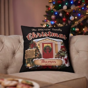 May include: A black square throw pillow featuring a printed graphic of a house entrance with a red door, a wreath, and Christmas trees. The text reads The BROWW Family Christmas, Thomas, and 2027. The design includes wooden sign accents.