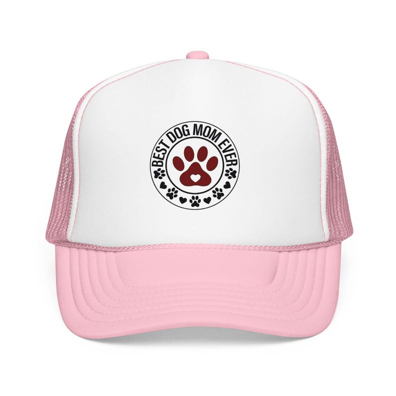 May include: A pink and white trucker hat with a curved brim. The hat features a circular design with the text "BEST DOG MOM EVER" surrounding a paw print and heart graphic. The hat has a mesh back.