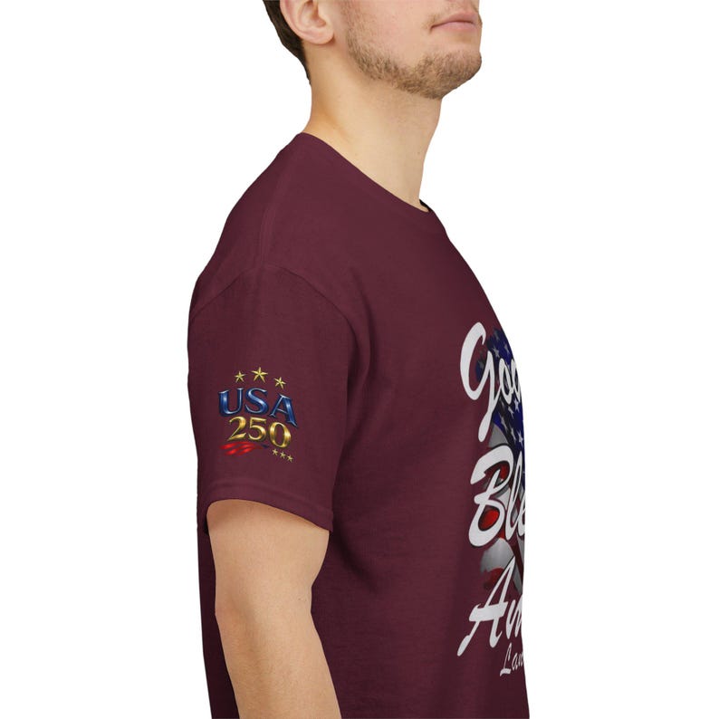 May include: Maroon t-shirt with the text "God Bless America" in white script and a partial American flag design. The left sleeve features the text "USA 250" with stars.