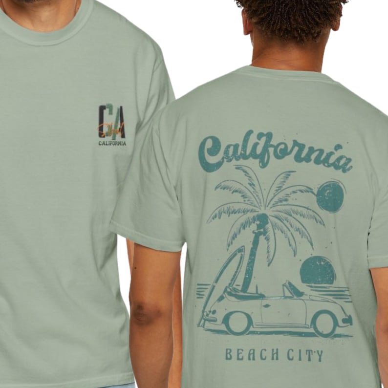 May include: A sage green short-sleeve t-shirt featuring a small CA California logo on the front chest. The back displays a graphic of a convertible car, a surfboard, a palm tree, and two suns with the text California Beach City in dark green.