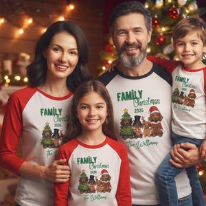 Op de afbeelding: Bijpassende witte en rode raglan-shirts met een afbeelding van vier teckels in feestelijke kleding, met de tekst "FAMILY Christmas 2026" en "The Williams" op de voorkant gedrukt. De shirts hebben lange rode mouwen en een witte romp.