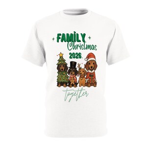 Puede incluir: Una camiseta blanca con un gr&aacute;fico de cuatro perros salchicha y el texto "FAMILY Christmas 2026" y "together". Los perros llevan ropa festiva, incluyendo un disfraz de &aacute;rbol de Navidad, un sombrero de copa con bufanda, astas de reno y un traje de Santa.