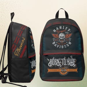May include: A black backpack featuring Harley-Davidson branding with a skull and wings graphic, the text "BORN TO RIDE" and "AMERICAN LEGEND," and the name "Thomas" printed in gold script on the side panel with red accent stripes.
