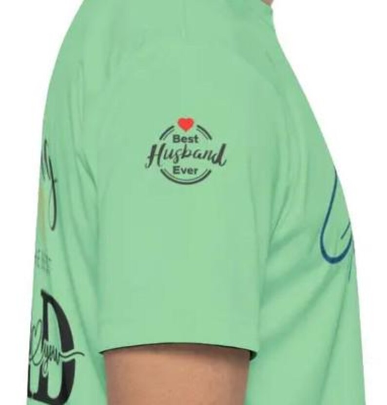 Pu&ograve; includere: Maglietta verde chiaro con la scritta "Best Husband Ever" in un design circolare con un cuore rosso. La maglietta presenta anche la parola "Dad" in un font grande.