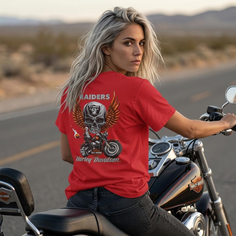 K&ouml;nnte beinhalten: Ein rotes Kurzarm-T-Shirt mit einem Grafikdruck auf der R&uuml;ckseite. Das Motiv zeigt einen gro&szlig;en Totenkopf mit einem Raiders-Logo-Helm und Fl&uuml;geln &uuml;ber einem Motorrad. Der Schriftzug lautet RAIDERS und Harley Davidson in wei&szlig;er Schrift.