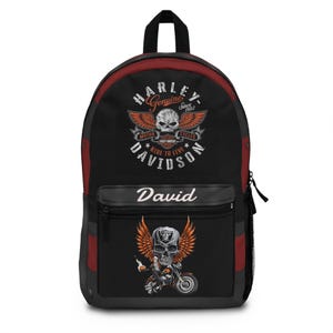 May include: A black backpack with red side panels featuring a Harley-Davidson logo with a skull and wings on the top section. The front pocket displays the name David in white script above a graphic of a skull with wings riding a motorcycle.