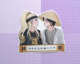 May include: A sticker featuring two illustrated figures, one with blonde hair wearing a black and gold patterned outfit and a black headband, and the other with black hair wearing a grey shirt and a straw hat. The sticker has a gold banner with the text "DAECHWITA" and a black and white logo.