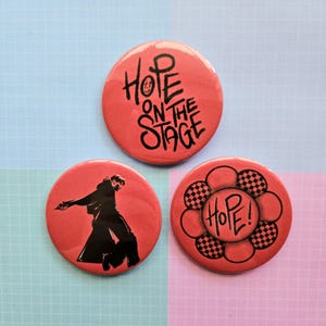 Könnte beinhalten: Drei rote runde Anstecknadeln mit schwarzem Text und Bildern. Die erste Nadel zeigt den Text "Hope on the Stage" in schwarzer Graffiti-Schrift. Die zweite Nadel zeigt eine schwarze Silhouette einer tanzenden Person. Die dritte Nadel hat eine schwarz-weiß karierte Blume mit dem Wort "Hope!" in der Mitte.