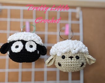 May include: Two crocheted sheep ornaments hanging from a white grid. One sheep is black with white eyes and a white face. The other sheep is tan with white eyes and a white face. Both sheep have white wool.