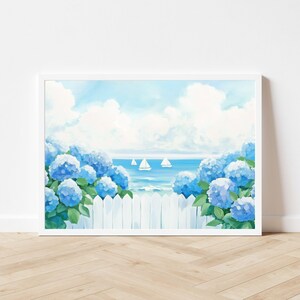 May include: A framed art print depicts a coastal scene. Blue hydrangea bushes frame a white picket fence, with sailboats on the ocean under a cloudy sky. The artwork is in a white frame.