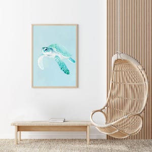 Puede incluir: Una impresi&oacute;n enmarcada de una pintura de acuarela de una tortuga marina nadando en un oc&eacute;ano azul claro. La tortuga es verde y azul con un caparaz&oacute;n blanco. La impresi&oacute;n est&aacute; colgada en una pared blanca en una habitaci&oacute;n con una silla colgante de mimbre y un banco de madera.