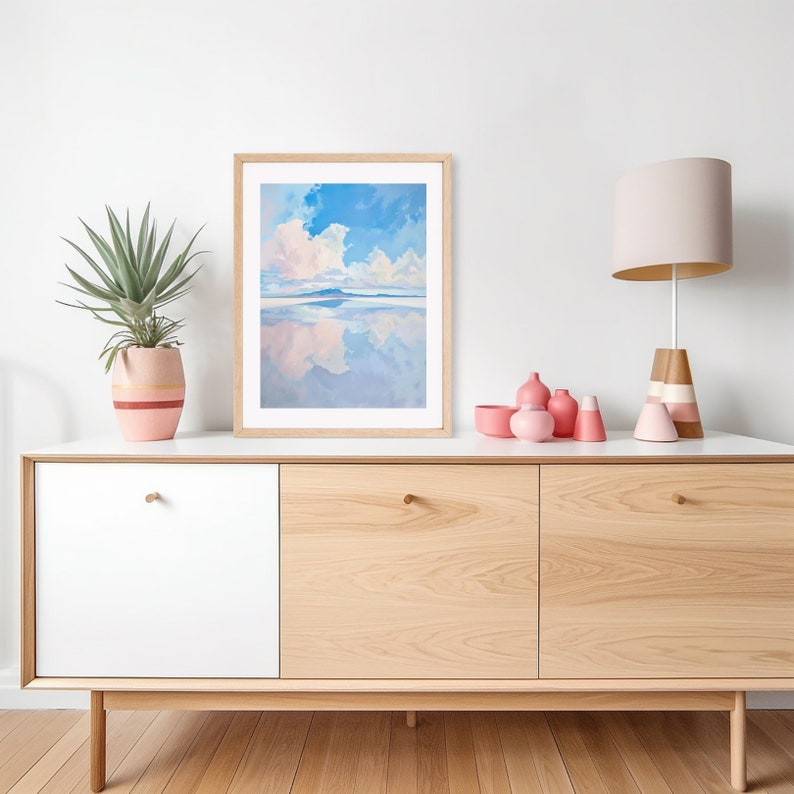 May include: A framed painting of a blue sky with white clouds reflected in a body of water. The painting is hanging on a light wood cabinet with two white doors and two wood doors. There are pink ceramic vases on the cabinet.