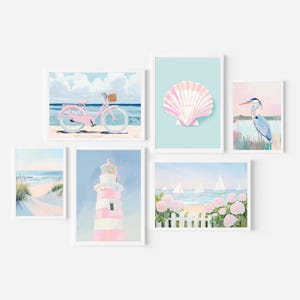 Peut inclure: Une collection d'impressions d'art aquarelles encadrées représentant des scènes côtières. Les impressions représentent un vélo rose sur une plage, un coquillage, un phare, un héron, une scène de plage et des voiliers. La palette de couleurs comprend des nuances de rose, de bleu et de blanc.