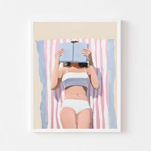 May include: A woman in a white bikini lies on a pink and blue striped beach towel, reading a blue book.