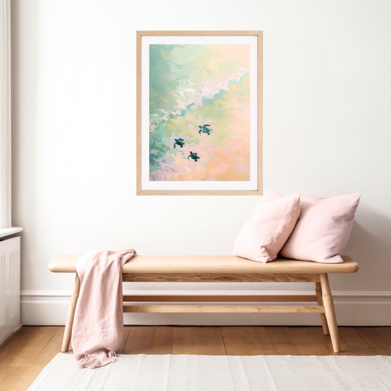 Puede incluir: Una pintura enmarcada de tres tortugas marinas nadando en un oc&eacute;ano turquesa y rosa. La pintura est&aacute; en un marco de madera claro y est&aacute; colgada en una pared blanca.
