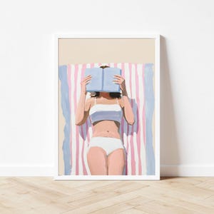 May include: A woman in a white bikini lies on a pink and blue striped beach towel, reading a blue book.