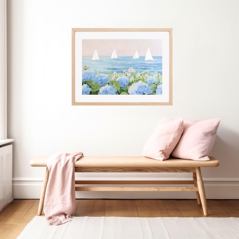 Pu&ograve; includere: Un dipinto ad acquerello incorniciato raffigura barche a vela su un mare blu, con ortensie blu in primo piano. Il dipinto &egrave; in una cornice di legno chiaro, appeso sopra una panca di legno con cuscini rosa e un plaid rosa.