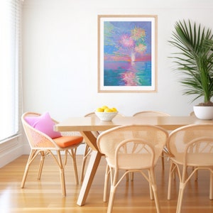 May include: A framed painting of fireworks exploding over a body of water. The painting is in a light wood frame and is hanging on a white wall. The wall is behind a dining table with four chairs. The table is made of wood and has a light wood finish. The chairs are made of wicker and have a natural finish. There are lemons in a bowl on the table.