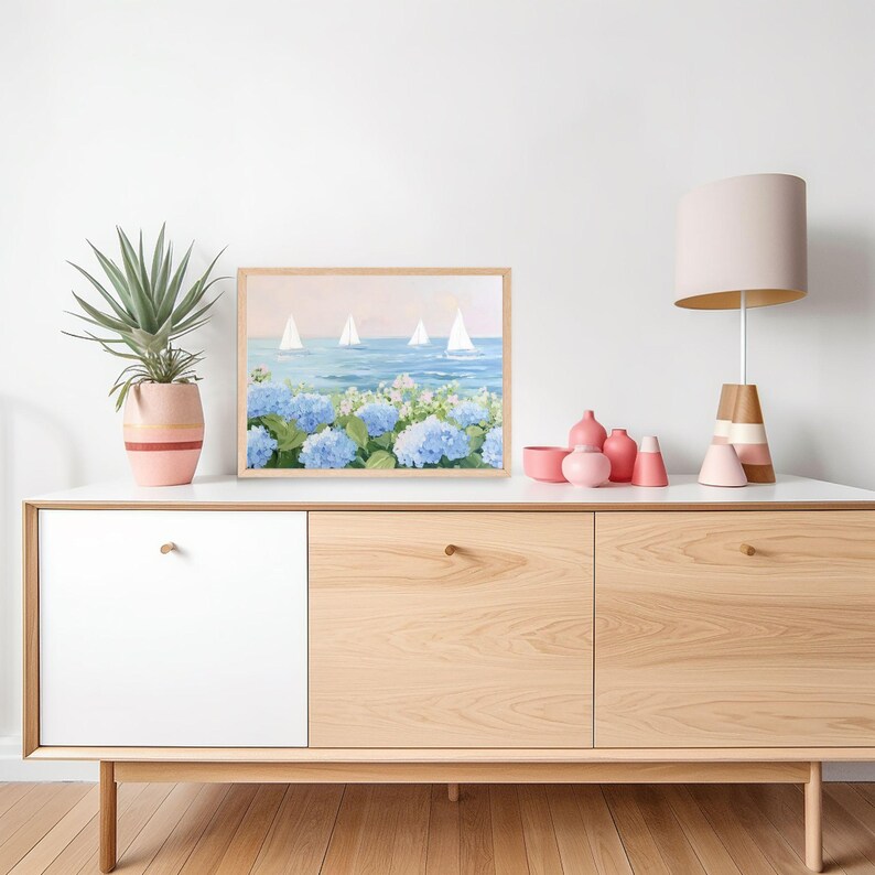 Pu&ograve; includere: Un dipinto incorniciato raffigura barche a vela su un mare blu con ortensie blu in primo piano. Il dipinto &egrave; su un mobile bianco e in legno, accanto a una pianta in vaso e vasi rosa. Una lampada con paralume beige e base a righe &egrave; anche sul mobile.