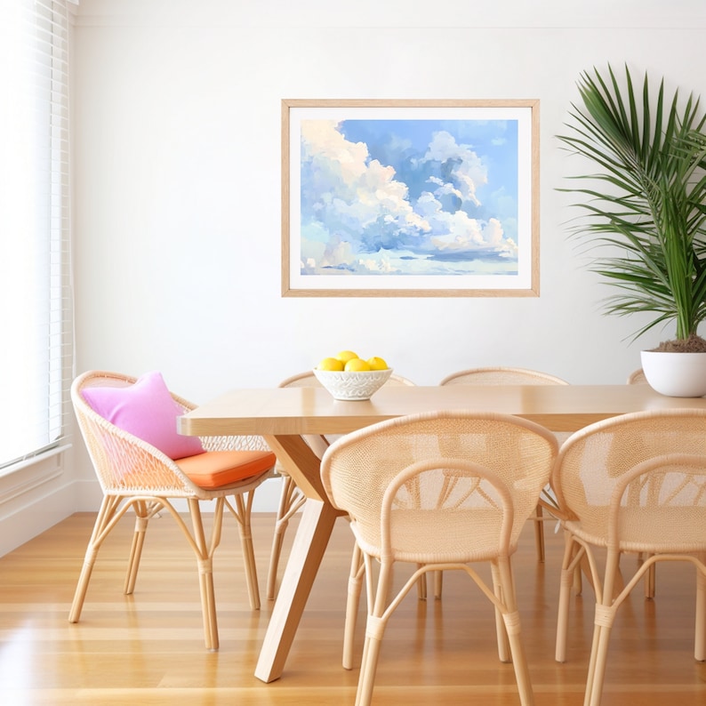 Puede incluir: Una pintura enmarcada de un cielo azul con nubes blancas. La pintura est&aacute; colgada en una pared blanca sobre una mesa de madera con cuatro sillas. Las sillas est&aacute;n hechas de mimbre y tienen un acabado natural. Hay un taz&oacute;n de limones en la mesa.