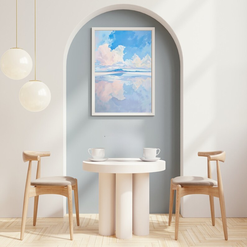 May include: A framed painting of a blue sky with white clouds reflected in a body of water. The painting is hanging on a light blue wall in a room with a white table and two wooden chairs.