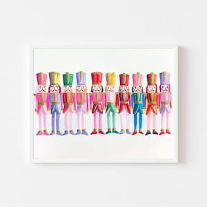 Könnte beinhalten: Ein gerahmter Druck mit einer Reihe farbenfroher Nussknackersoldaten. Jeder Soldat hat eine einzigartige Uniform mit rosa, blauen, grünen, roten und gelben Akzenten. Das Kunstwerk ist vor einem weißen Hintergrund platziert.