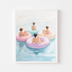 May include: A framed art print depicts four people relaxing in a pool on colorful inflatable rings. The artwork features a light blue water background and the people are wearing swimsuits in pastel colors. The inflatable rings are pink, yellow, and teal.