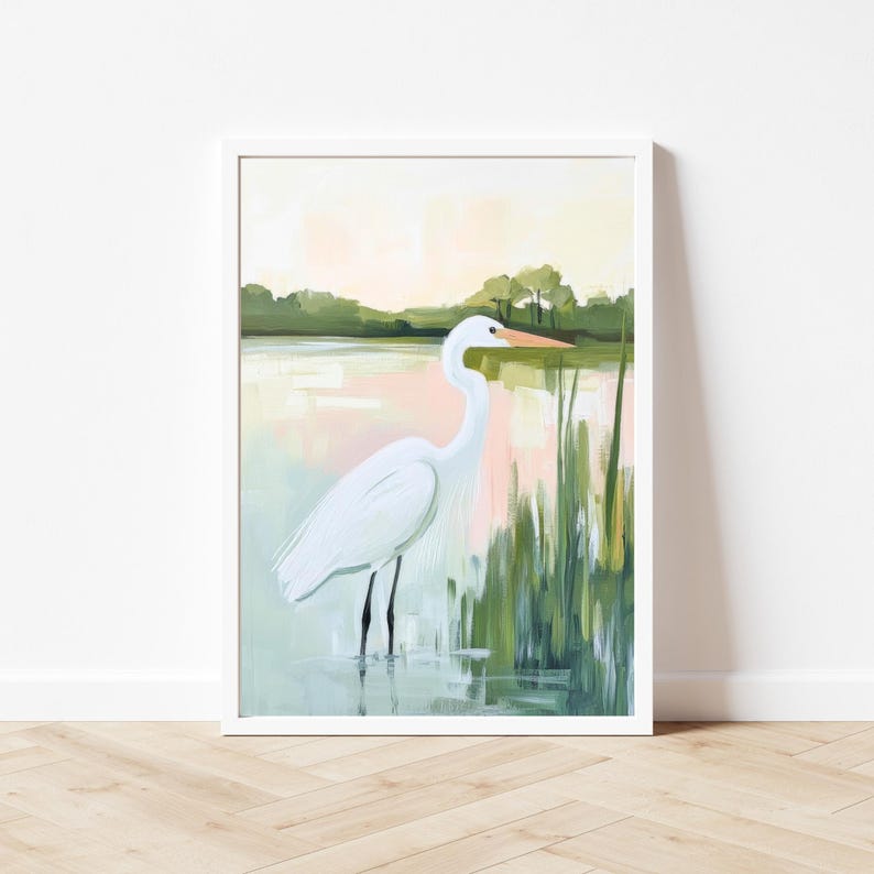 K&ouml;nnte beinhalten: Gerahmter Kunstdruck eines Graureihers im Wasser. Das Gem&auml;lde zeigt eine ruhige Landschaft mit sanften Rosa- und Gr&uuml;nt&ouml;nen, Schilf und einem verschwommenen Hintergrund von B&auml;umen. Der Vogel hat einen langen Hals und einen orangefarbenen Schnabel.