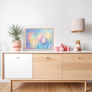 May include: A framed art print featuring a colorful fireworks display in shades of yellow, pink, and blue. The artwork is displayed on a white cabinet with a wooden frame, alongside a potted plant and decorative items.