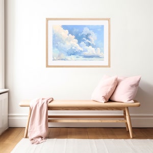Puede incluir: Una pintura enmarcada de un cielo azul con nubes blancas y esponjosas. La pintura est&aacute; colgada en una pared blanca sobre un banco de madera con almohadas de color rosa.