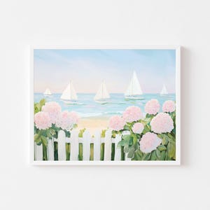 Op de afbeelding: Een ingelijst schilderij toont een kustlandschap met zeilboten op het water. Roze hortensia's bloeien voor een witte hek. De lucht is lichtblauw en het water turquoise.