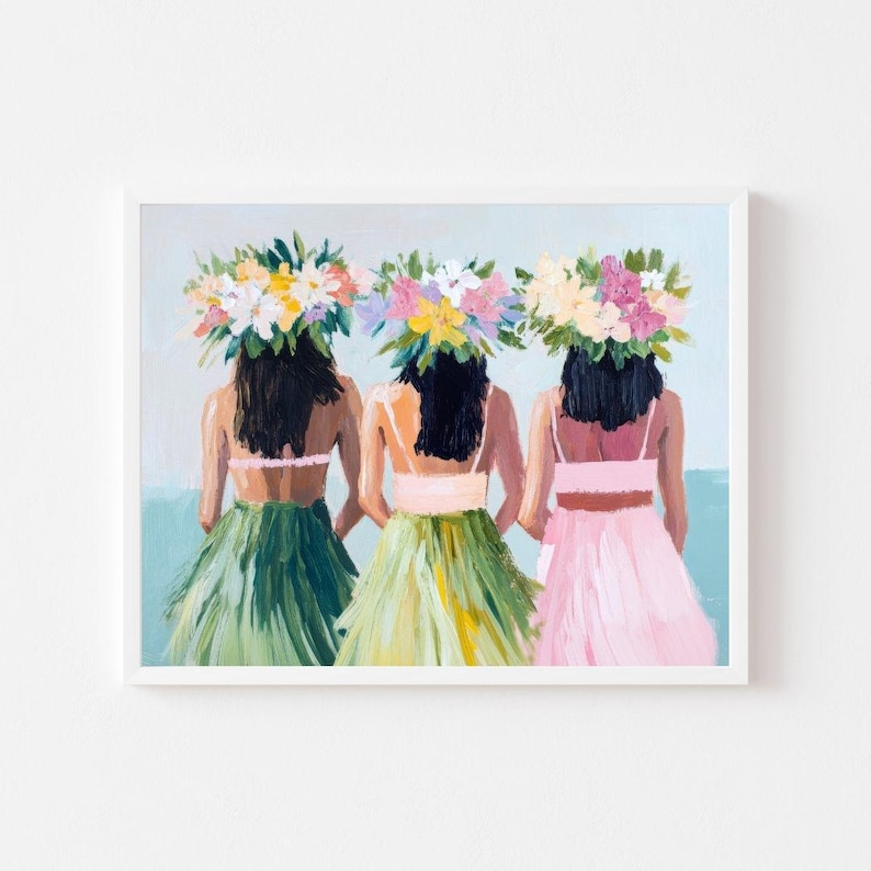 Op de afbeelding: Drie vrouwen met bloemenkransen en kleurrijke rokken staan ​​met hun rug naar de kijker. De vrouwen bevinden zich op een strand met een blauwe lucht en zee op de achtergrond.